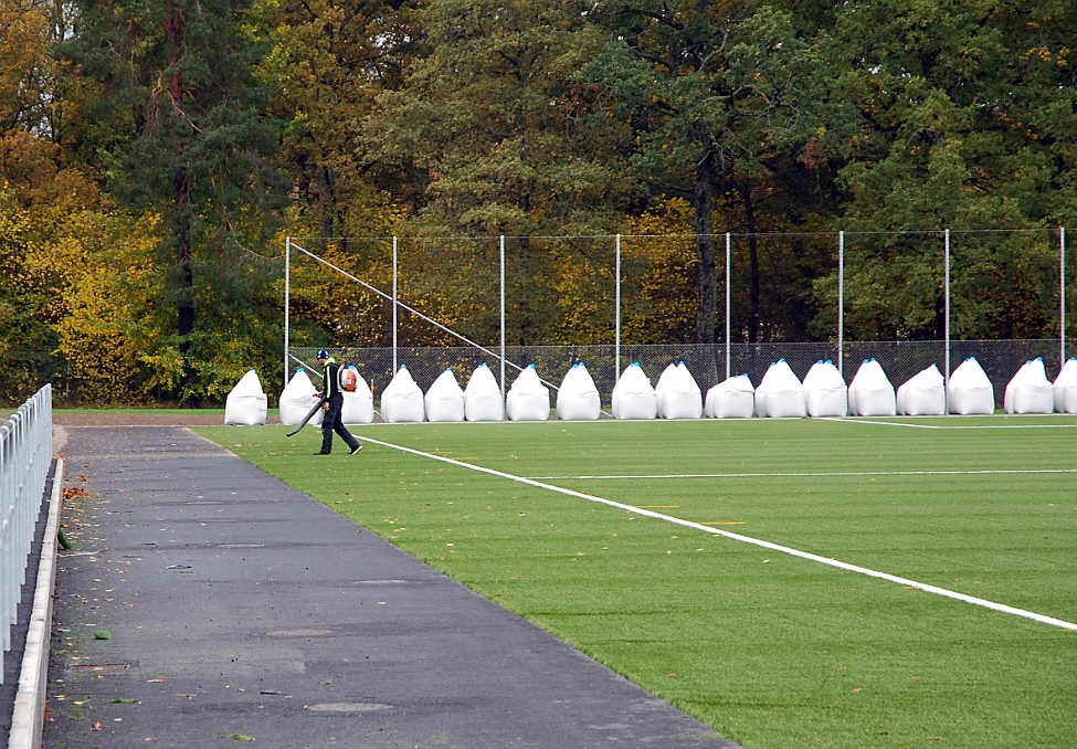 2014_1008_115758AA.JPG - Man blåser rent gräset innan gruset skall läggas ut på mattan
